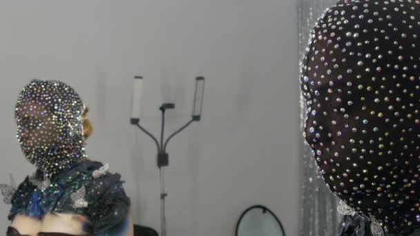 De alta moda. Modelo na imagem de uma menina alienígena em uma máscara preta em strass espumantes, brilhos, borboletas de metal em um fundo preto e prata posando na frente do estúdio do espelho
 - Filmagem, Vídeo