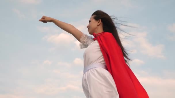 meisje droomt ervan om een superheld. mooie superheld meisje permanent op een veld in een rode mantel, mantel wapperen in de wind. Slow-motion. jonge vrouw speelt in een rode mantel met expressie van dromen. - Video