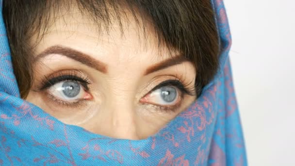 Retrato de una mujer adulta árabe de mediana edad con unos ojos azules hermosos e inusuales con pestañas largas en paño islámico tradicional niqab o burka azul. Primer plano de la hermosa mujer musulmana
 - Metraje, vídeo