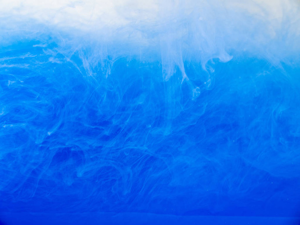 Daling van acryl inkt opgelost in water, close-up. Abstracte achtergrond. Blauwe verf in vloeistof. Acryl wolken wervelende in water. Blauwe inkt golven in vloeibare, abstracte patroon. Onscherpe achtergrond. - Foto, afbeelding