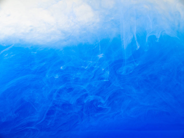 Blue acrylic ink dissolving into water, close up. Abstract background. Blue paint in liquid. Abstract acrylic clouds in liquid. Ink waves in water, abstract pattern. Blurred background. - Fotoğraf, Görsel