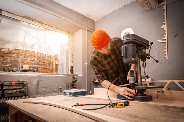 Ένας άνθρωπος με ρούχα εργασίας και ενός ξυλουργού ΚΓΠ σκάλισμα ξύλινη σανίδα σε ένα σύγχρονο μεγάλο γεωτρήσεων μηχάνημα σε ένα ανοιχτό εργαστήριο - Φωτογραφία, εικόνα
