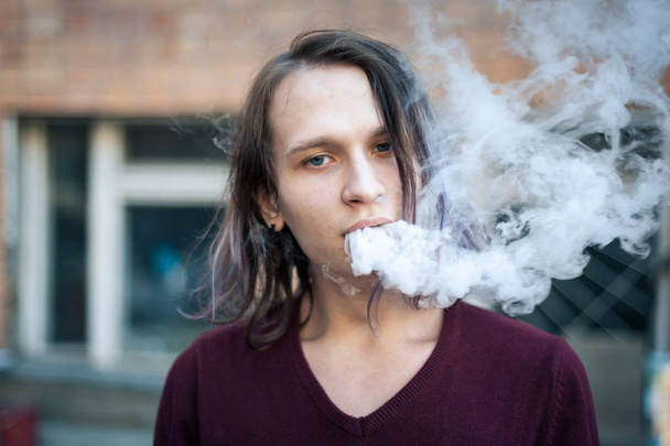 Portret van een jonge man in de rook van sigaretten - Foto, afbeelding