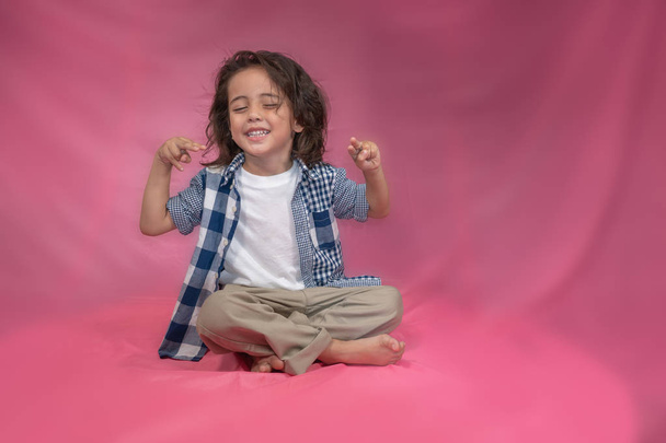 ένα ευτυχισμένο αγόρι με μακριά μαλλιά που κάθεται σε ροζ φόντο - Φωτογραφία, εικόνα