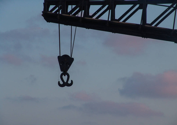 Sunset view of a metal double hook hanging with ropes from a tal - Photo, Image