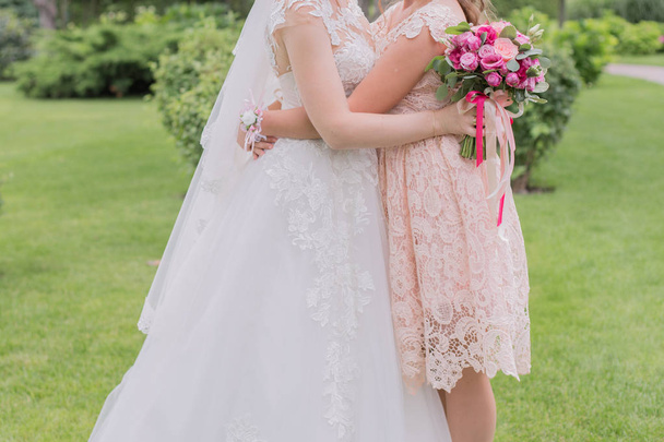 bride with bridesmaid and wedding bouquet in the park - Фото, зображення