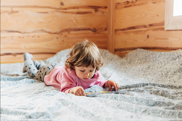 toddler girl is reading book in bed. - Fotoğraf, Görsel
