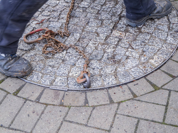Legs on a lifting a heavy manhole cover - Photo, Image