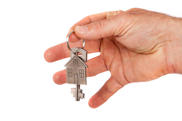 Man's hand giving a new metal key with home shaped keychain, isolated. New home concept - 写真・画像