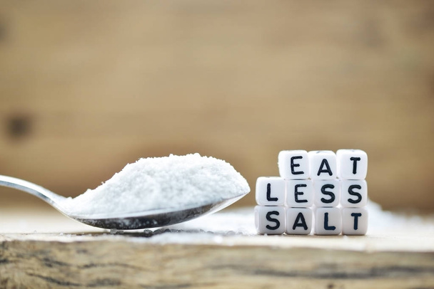 Comer menos mensaje de sal escrito cerca de cuchara de madera llena de sal granulada y agitador sobre fondo rústico
 - Foto, imagen