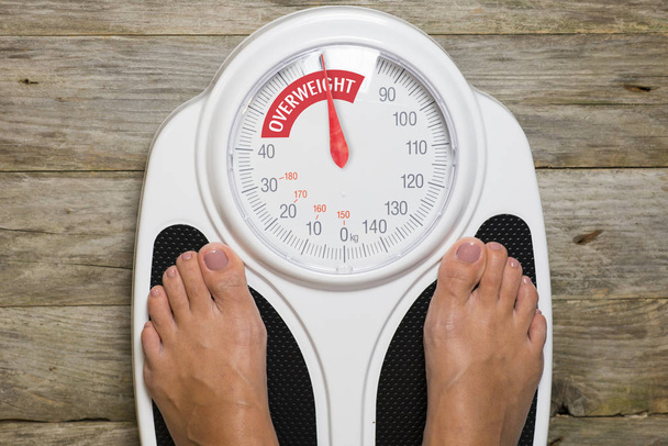 Mulher jovem em pé na escala de peso analógico clássico indicando excesso de peso
 - Foto, Imagem