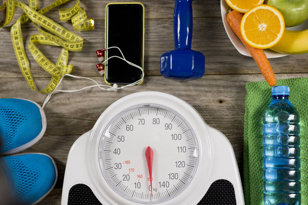 Аналоговая весовая шкала, спортивный объект и здоровые фрукты на деревянном фоне, концепция здорового образа жизни
 - Фото, изображение