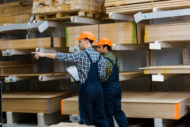 warehouse worker pointing with finger while standing near indian friend - Photo, Image