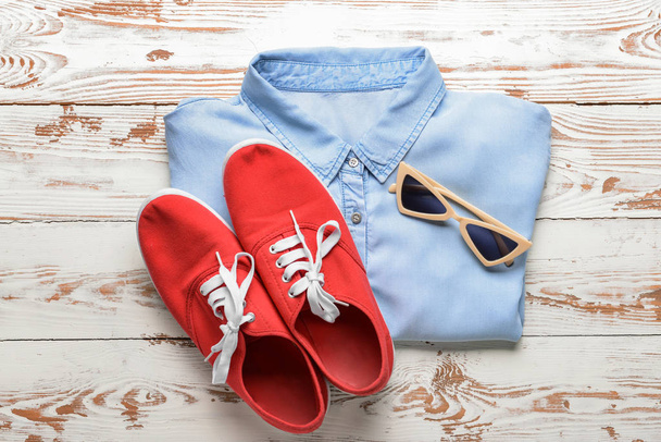 Camicia con scarpe da ginnastica e occhiali da sole su sfondo bianco in legno
 - Foto, immagini