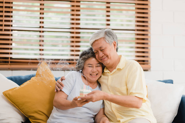 Asian elderly couple man holding cake celebrating wife's birthday in living room at home. Japanese couple enjoy love moment together at home. Lifestyle senior family at home concept. - Photo, image