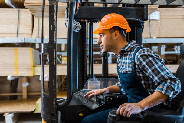 concentrated handsome worker in uniform and helmet operating forklift machine - Photo, Image