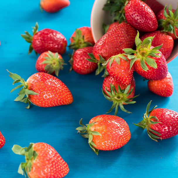 fresh bright strawberries spilled out of the bowl on a blue background - 写真・画像