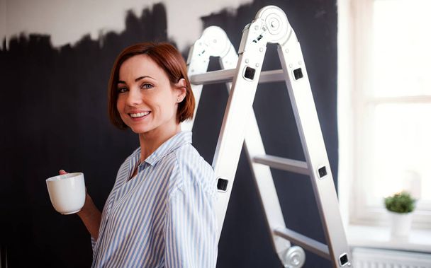 A portrait of young woman painting wall black. A startup of small business. - Фото, изображение