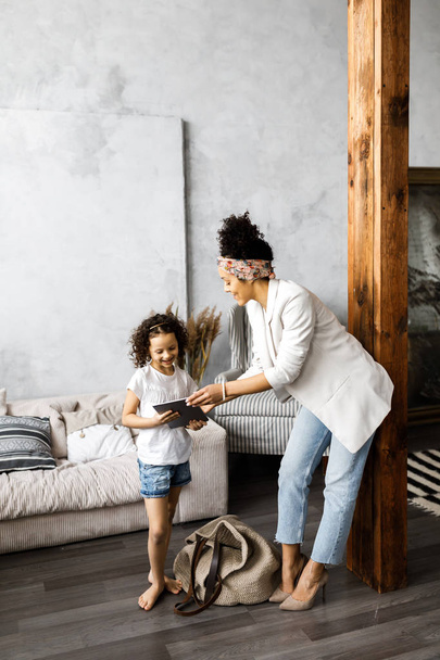 Una simpatica madre e figlia parlare e guardare il tablet mentre in piedi in soggiorno
 - Foto, immagini