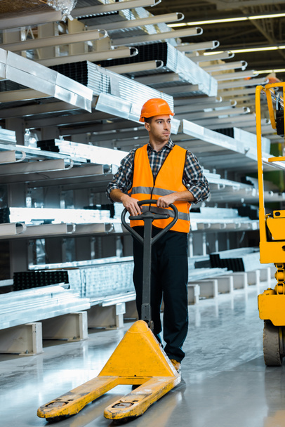 handsome, serious warehouse worker standing near pallet jack - Photo, Image