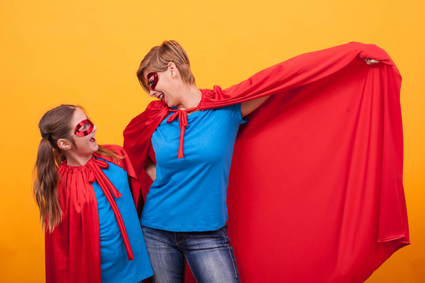 Moeder en dochter gekleed als superheros verlijmen op gele achtergrond - Foto, afbeelding
