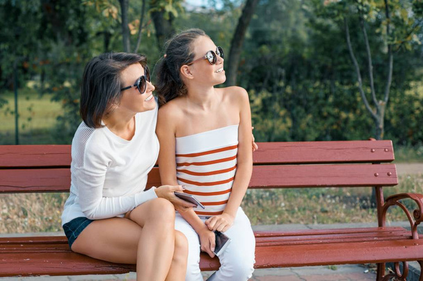Communication entre le parent et l'enfant. Maman et fille adolescente parlent et rient assis sur le banc dans le parc
 - Photo, image