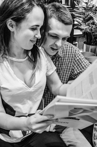 Young married loving couple sit and read the magazine. Happy emotions. Thumb through the brochure and choose goods for the house. - Foto, imagen