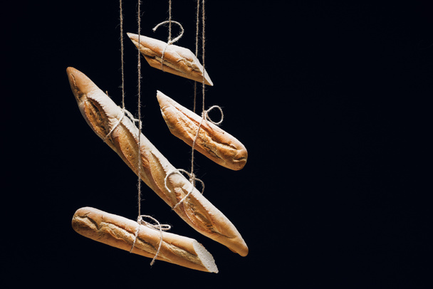 loaves of fresh baked baguettes on ropes isolated on black - Фото, зображення