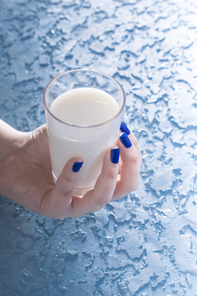 partial view of woman holding glass of milk on blue background - Photo, Image