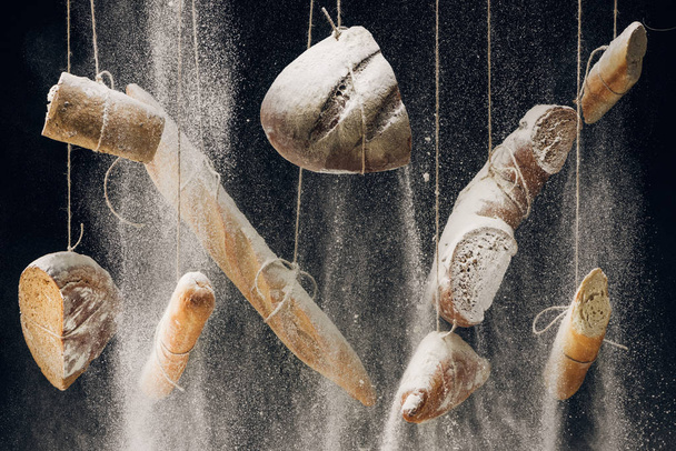 flour falling at bread, baguettes and croissant hanging on ropes on black background - Photo, Image