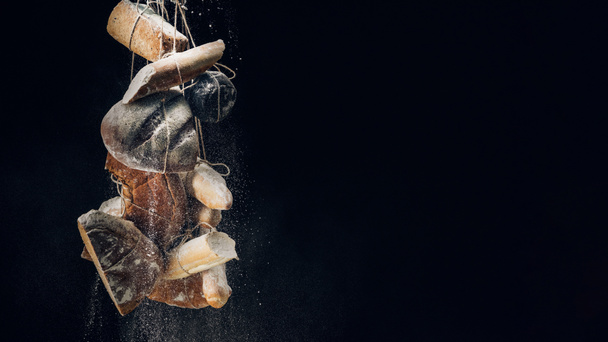 white flour falling at loaves of bread, baguettes and croissant on ropes on black background with copy space - Photo, Image