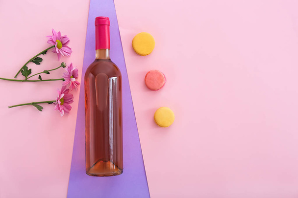 花と色の背景上のマカロンとワインのボトル - 写真・画像