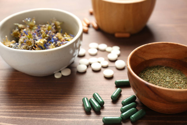 Plant based pills and bowls with dry herbs on wooden background - Foto, Bild