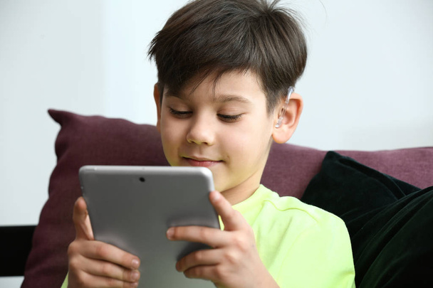 Petit garçon avec prothèse auditive utilisant une tablette à la maison
 - Photo, image