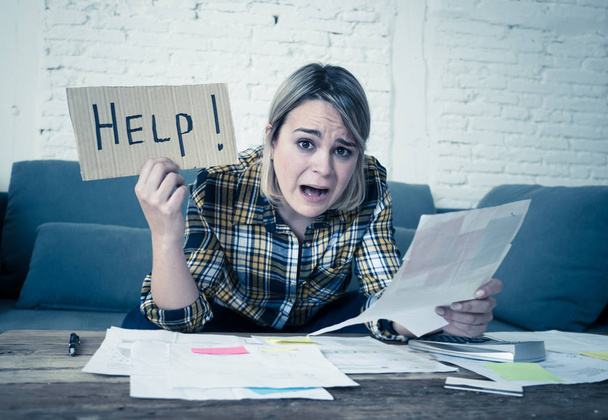 Lifestyle portrait of worried desperate young woman feeling stressed while working through finances at home showing Help sign. In single mother paying off debts and bills and financial problems. - Foto, Imagen