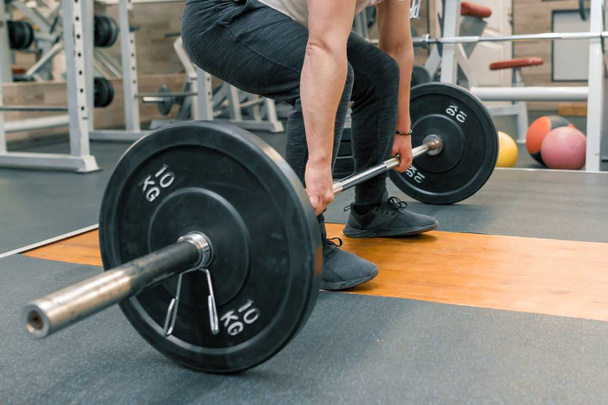 Closeup of arms and legs of man exercising with barbell at sport gym. Athlete, bodybuilding, training, weightlifting, workout exercises concept - Valokuva, kuva