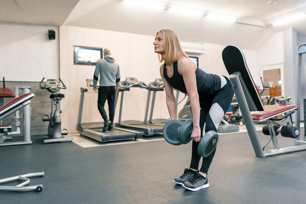 Young beautiful blond woman doing strength exercises with dumbbells in gym. Sport, fitness, bodybuilding, training, workout exercises concept - Foto, Bild