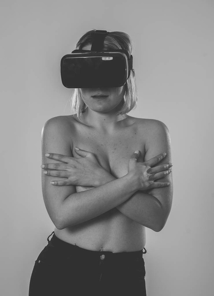Curious sensual woman using augmented or virtual reality glasses, feeling excited about simulation, exploring virtual sexuality while getting topless covering her breast. In virtual reality concept. - Zdjęcie, obraz