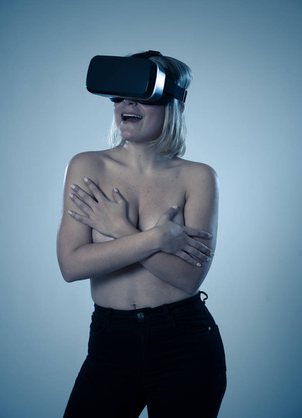 Sensual attractive woman using augmented or virtual reality goggles feeling excited exploring virtual sexuality while getting topless covering her breast. In cyber sex VR simulator and new technology. - Zdjęcie, obraz