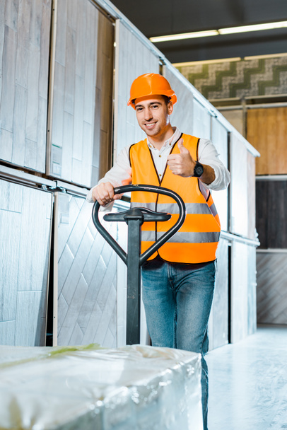 smiling worker carrying pallet jack and showing thumb up - Photo, Image