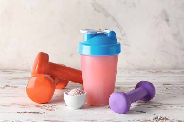 Bottle of protein shake with dumbbells on white wooden table - Foto, Bild