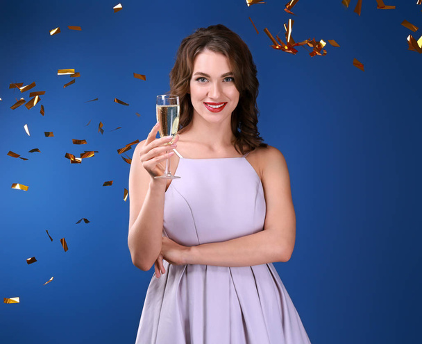 Beautiful young woman with glass of champagne and falling confetti on color background - Foto, Imagem