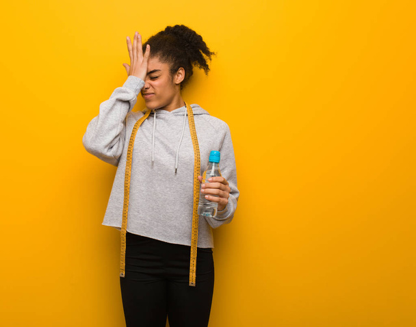 Mladí fitness černá žena zapomnětlivý, uvědomit si něco. Drží láhev s vodou. - Fotografie, Obrázek