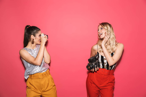 Image of two happy girls 20s in stylish outfit holding and photo - Valokuva, kuva