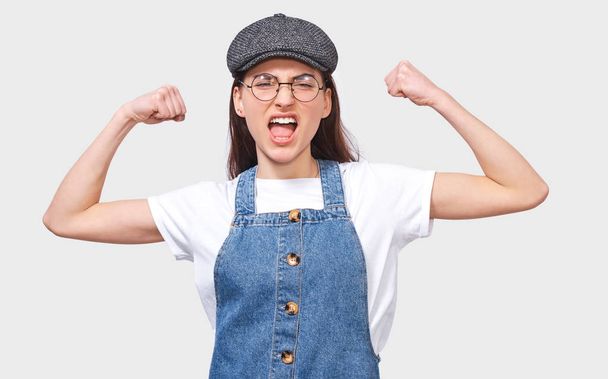 Portrait of furios young woman raises hands clenched in fists, screams with anger, isolated over white background, wears round transparent eyewear. Student girl has negative feelings and emotions. - Photo, Image
