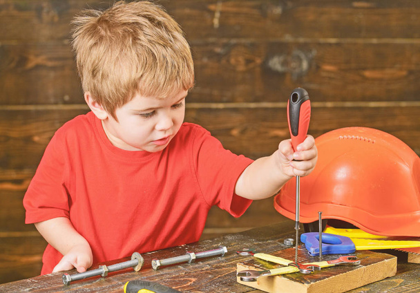 Blondes Kind spielt in Werkstatt. Junge bindet Schrauben an Holzbrett. Konzentriertes Kind lernt neue Fertigkeiten - Foto, Bild