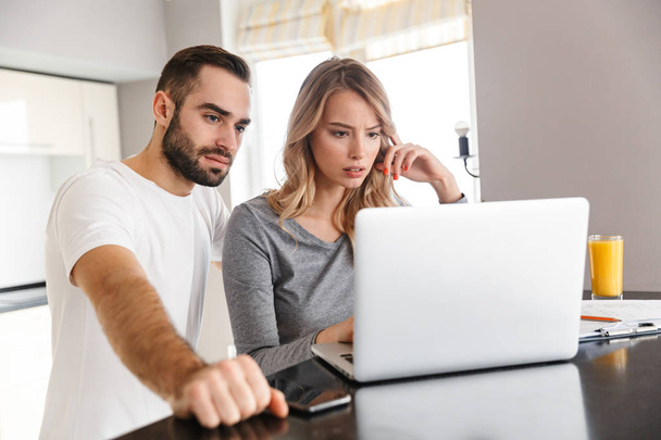 Young loving couple sitting at the kitchen using laptop computer. - Foto, Bild