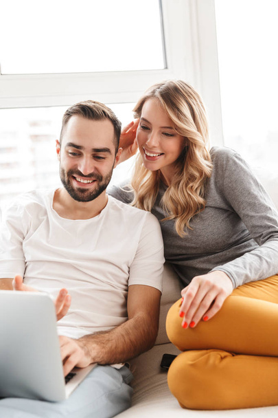 Amazing loving couple sitting indoors at home using laptop computer. - Foto, imagen