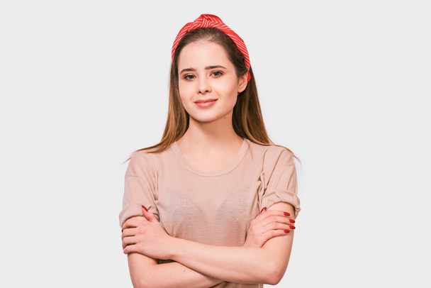 Beautiful European woman smiling, feels excitement, keeps hands crossed, posing against white background. Pretty female has joyful expression wearing red headband. - Foto, afbeelding