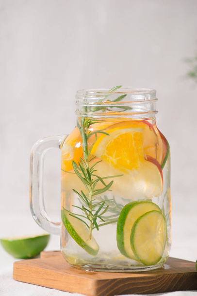 Water doordrenkt met limoen, sinaasappel, appel en rozemarijn. Koude detox zomer drankje. Selectieve aandacht - Foto, afbeelding